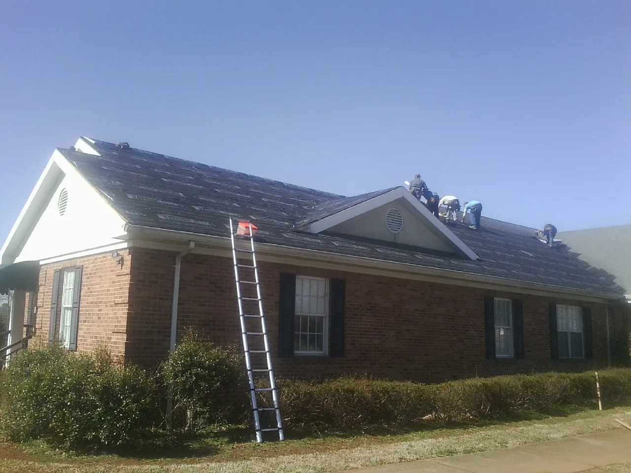 Crew tearing shingles off a brick ranch roof with a ladder set — Metal Roof Repair work by our crew in Thonotosassa