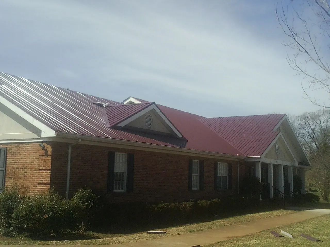 Red metal roof with gabled entries on a long brick building, from a Hail Damage Roof Repair job in Thonotosassa