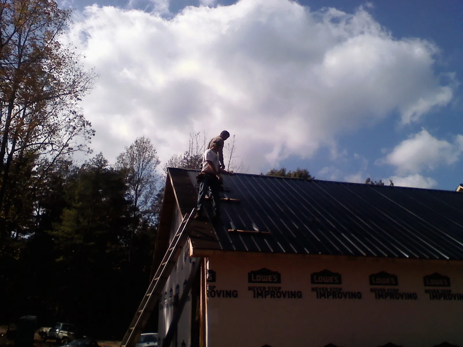 Roofer fastening dark metal panels high against a cloudy sky, from a Roof Inspection job in Thonotosassa