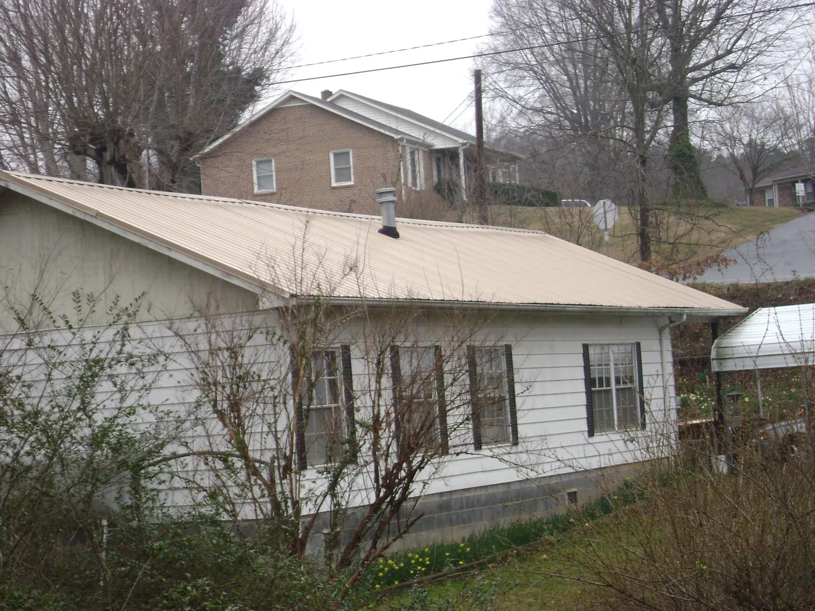 Tan metal roof on a white sided house set into a hillside — Commercial Roofing by Roofing Brothers in Thonotosassa